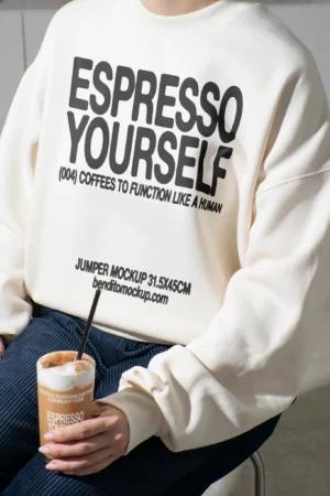 Person wearing an Espresso Yourself jumper while holding a cup of iced coffee