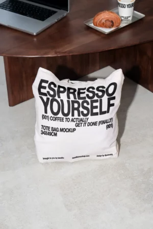 Espresso Yourself tote bag mockup on the floor next to a coffee table