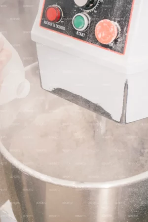 Water being poured into a dough mixer in a bakery setting.