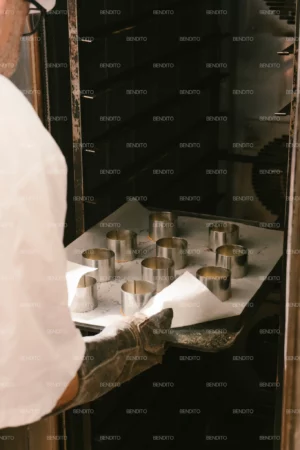 A baker placing a tray of pastry molds into a commercial oven.