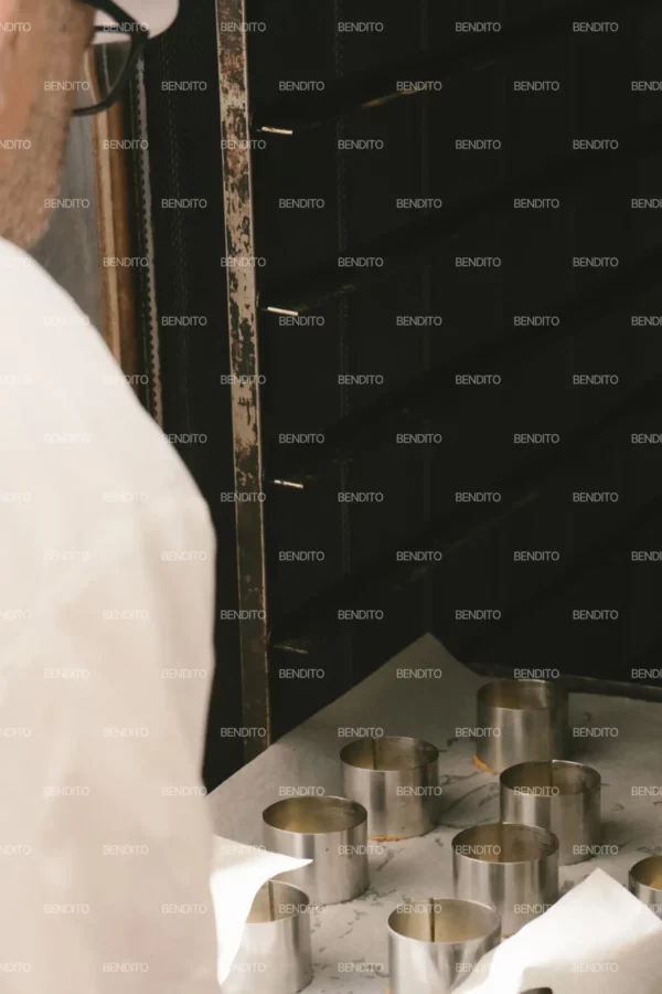 Zoom in of a baker placing a tray of pastry molds into a commercial oven.