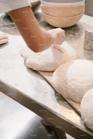A baker preparing artisan bread dough on a floured tray in a bakery.