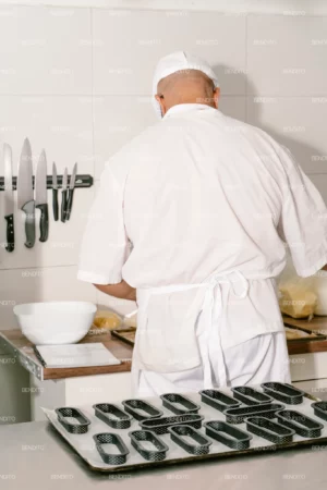 A baker arranging black perforated pastry molds on a tray in a professional kitchen.
