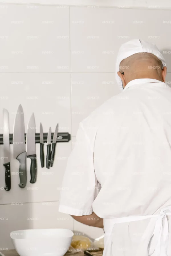 Zoom in of a baker arranging black perforated pastry molds on a tray in a professional kitchen.