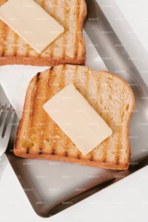Close-up of grilled toast with a slice of butter on a stainless steel tray.