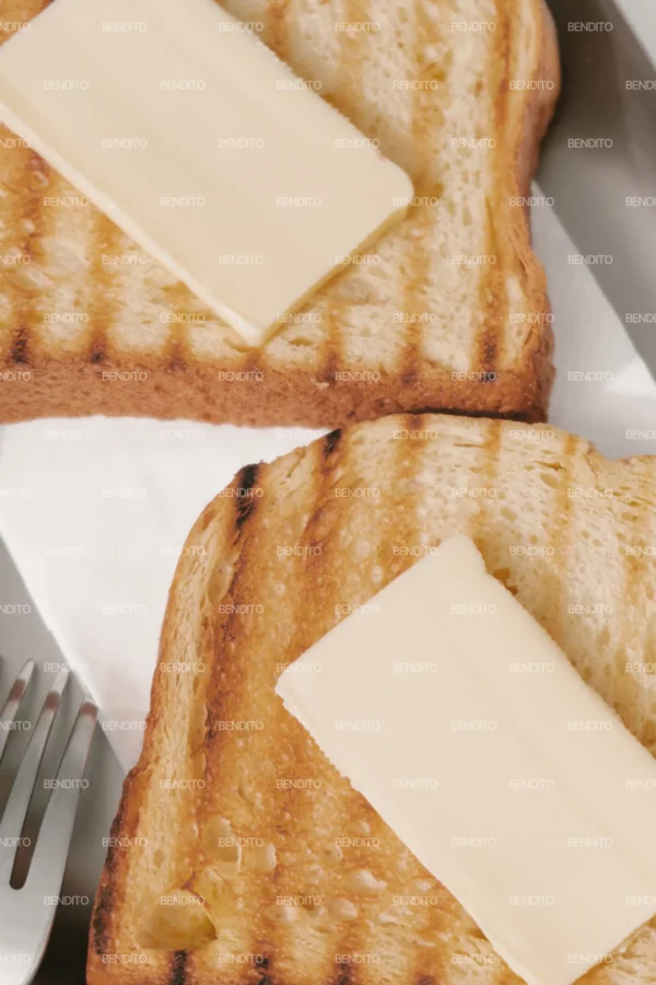 Zoom in of close-up of grilled toast with a slice of butter on a stainless steel tray.