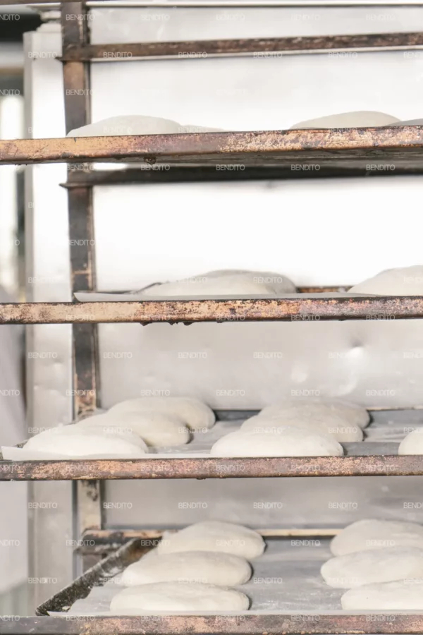 Zoom in of rows of proofing dough placed on metal bakery racks ready for baking.