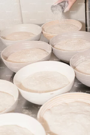 A hand sprinkling flour over dough in preparation for baking.