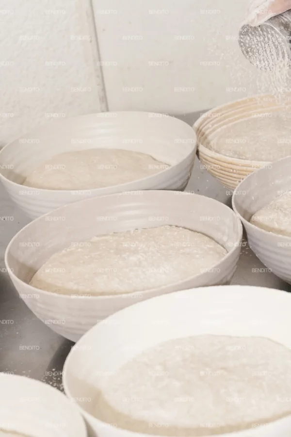 Zoom in of a hand sprinkling flour over dough in preparation for baking.