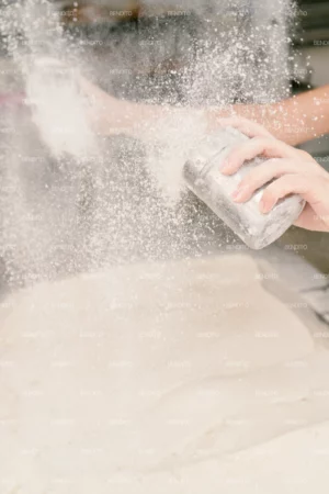 A baker sprinkling flour over bowls of proofing dough in preparation for baking.