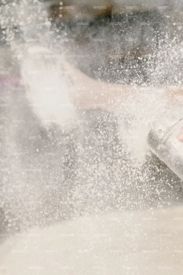Zoom in of a baker sprinkling flour over bowls of proofing dough in preparation for baking.