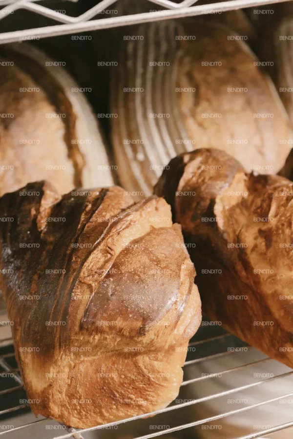 Zoom in of freshly baked artisan bread loaves cooling on racks in a bakery setting.