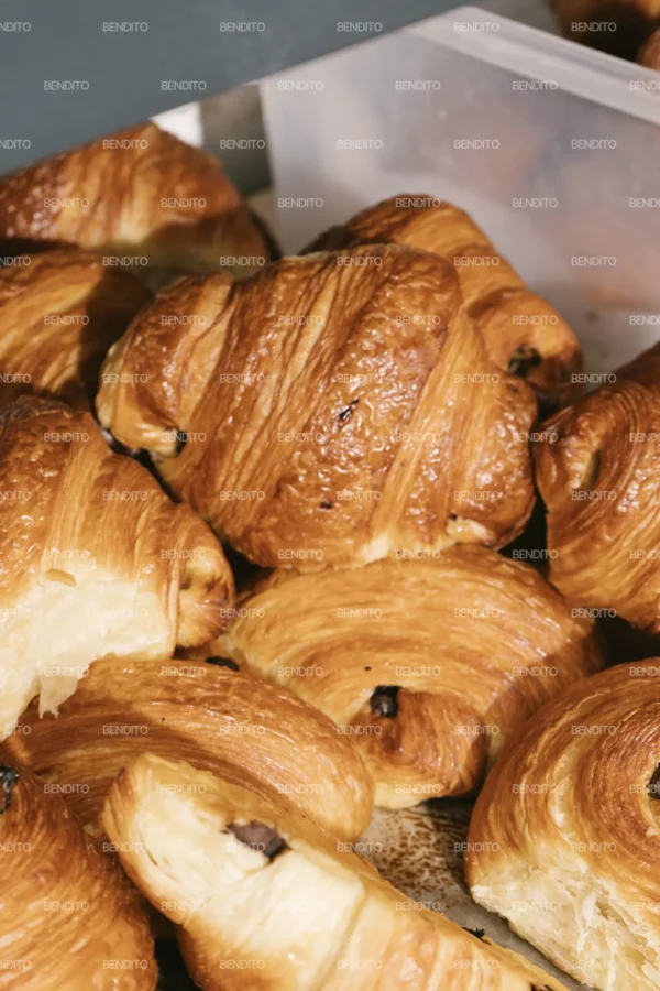 Zoom in of golden chocolate croissants displayed fresh from the oven in a bakery setting.