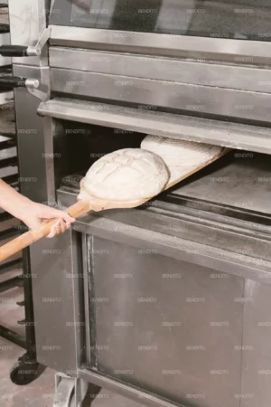 Artisan bread dough being placed into an industrial oven with a wooden peel.