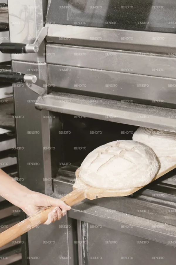 Zoom in of artisan bread dough being placed into an industrial oven with a wooden peel.
