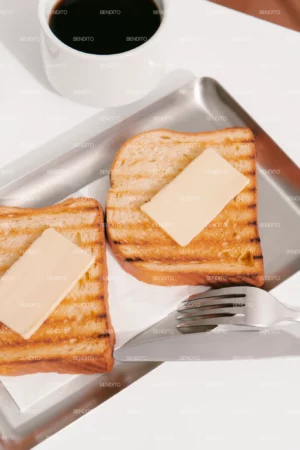 Two slices of grilled toast topped with butter served on a metal tray accompanied by coffee.