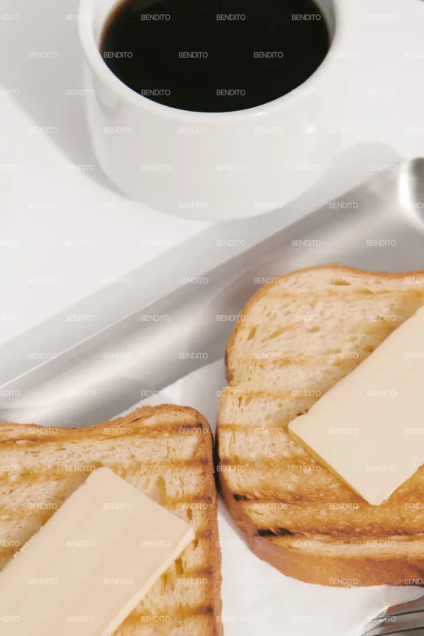 Zoom in of two slices of grilled toast topped with butter served on a metal tray accompanied by coffee.