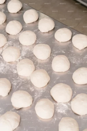 Rows of portioned dough balls placed neatly on a stainless steel counter.