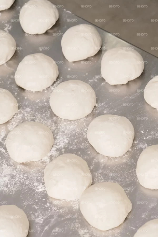 Zoom in of rows of portioned dough balls placed neatly on a stainless steel counter.