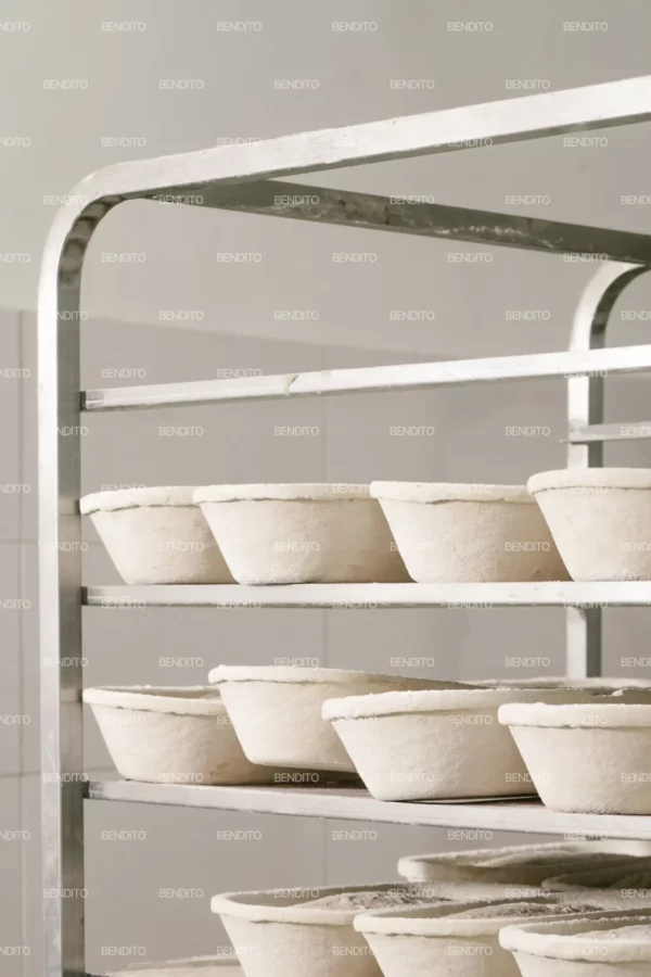 Zoom in of metal rack holding proofing dough loaves in traditional baskets.