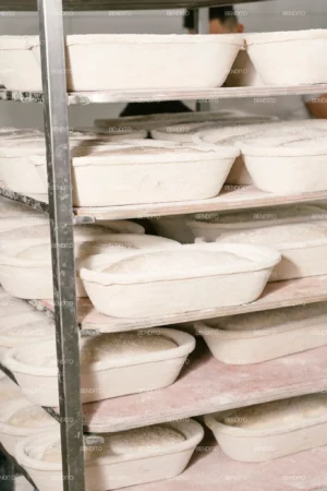 Artisan bread dough proofing in oval baskets on industrial bakery racks.