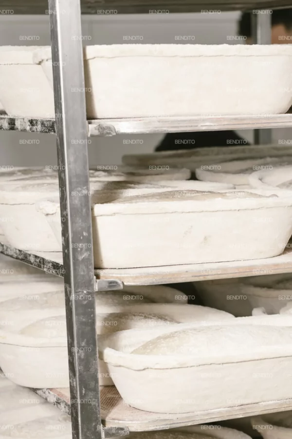 Zoom in of artisan bread dough proofing in oval baskets on industrial bakery racks.