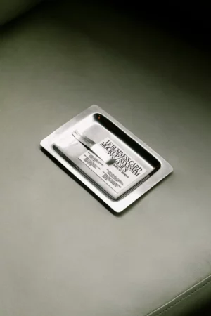 A business card mockup placed on a reflective metal tray, resting on a leather surface.