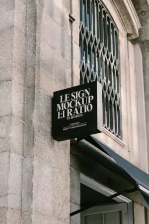 A black square signage mockup mounted on a stone wall, with holiday garlands in the background.
