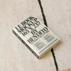 A hardcover book mockup with a blank cover is placed on a flat surface surrounded by soft shadows. The book's spine is visible and the lighting highlights the smooth texture of the cover.