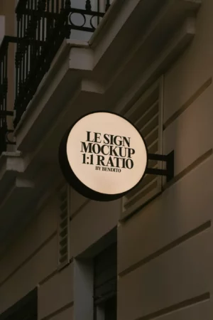 A mockup featuring a rectangular lightbox sign with a white background and black frame, displaying the text "Le Sign" in bold black letters. The sign is set against a plain and light gray wall. Even lighting highlights the smooth texture of the sign's surface.