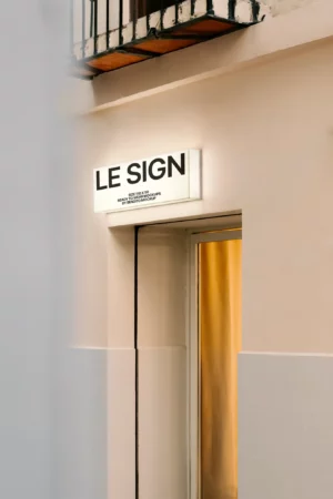 A mockup of a rectangular sign with a blank white surface mounted on a brick wall in a well-lit indoor setting.
