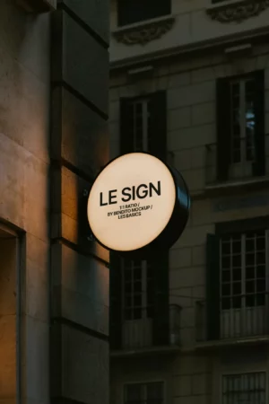 A mockup of a rectangular sign leaning against a white wall on a wooden floor with soft natural lighting.