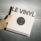 A mockup of a vinyl record cover displayed on a light wooden surface with a soft shadow cast to the right.