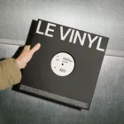 Hover image: A mockup of a vinyl record cover displayed on a light wooden surface with a soft shadow cast to the right.