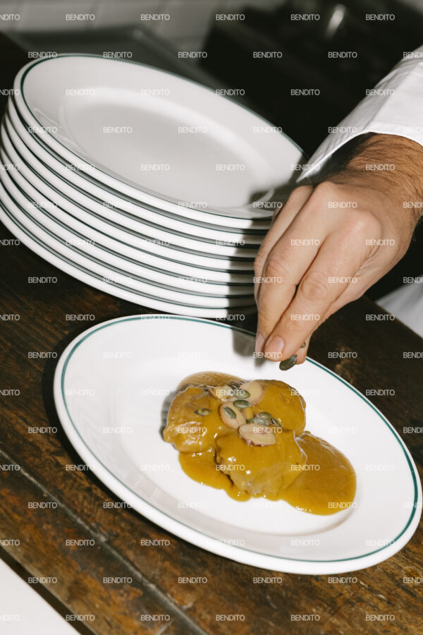 Close-up angle of a chef plating a gourmet dish with sauce.