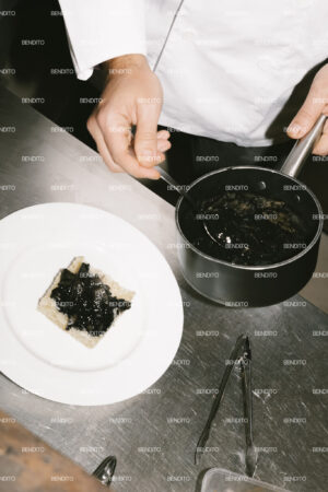 Chef plating a dish with sauce.