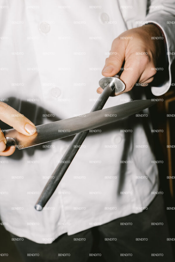 Close-up view of a chef sharpening a knife with a honing steel.