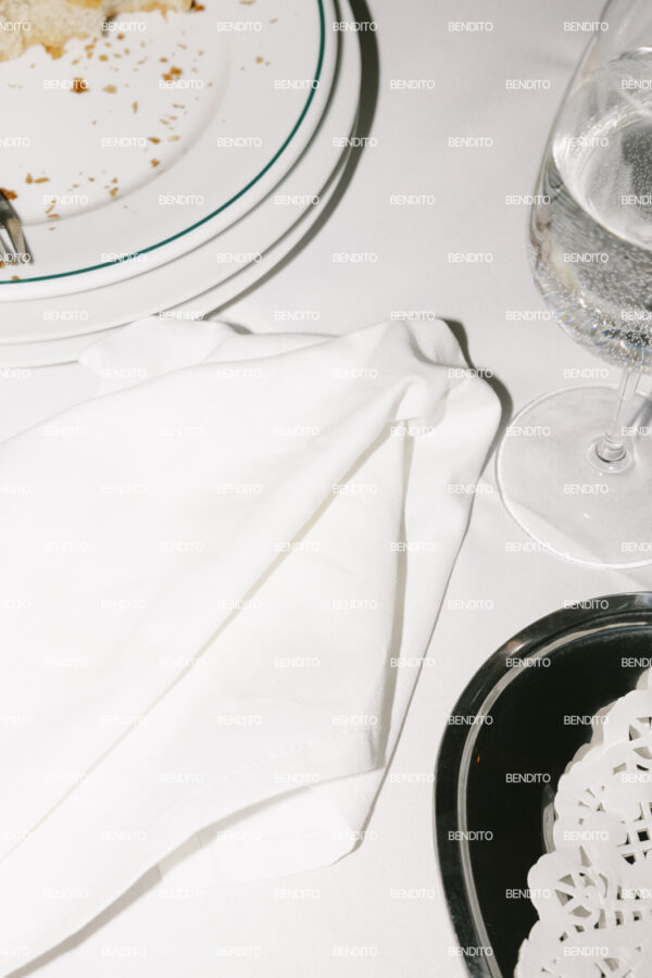 Close-up view of a restaurant table setting with white plates cutlery and a glass of water.