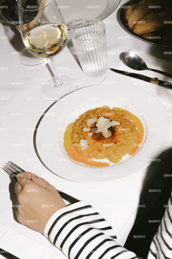 Tight crop of saffron risotto plated at a restaurant table with wine and bread.