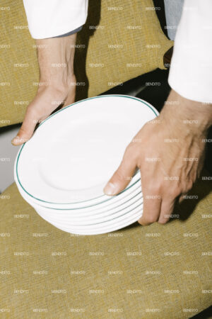 Hands holding stacked white plates.