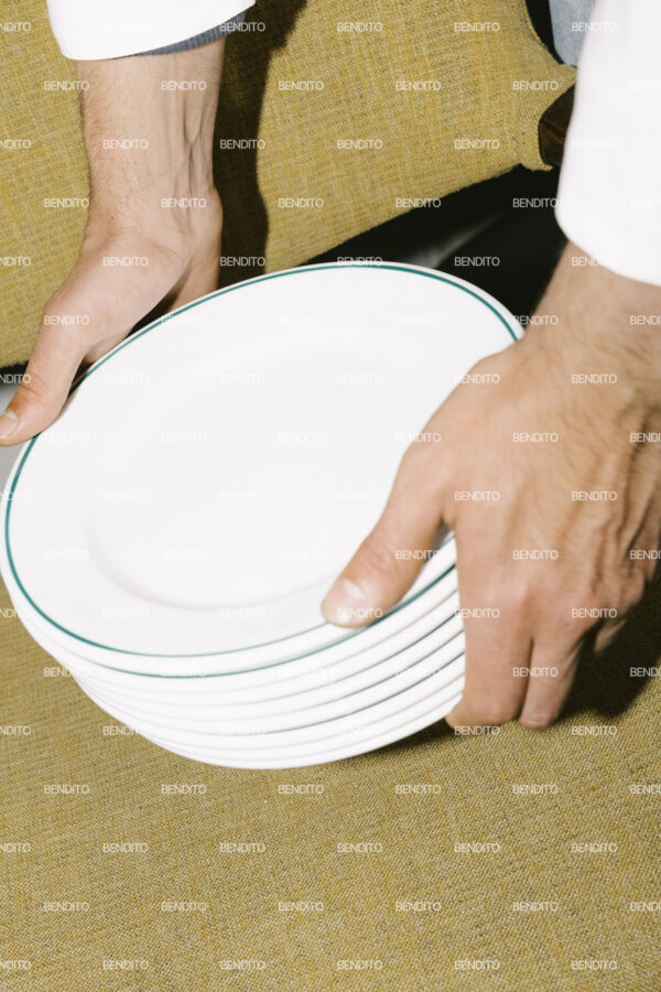 Tight crop of hands holding stacked white plates.