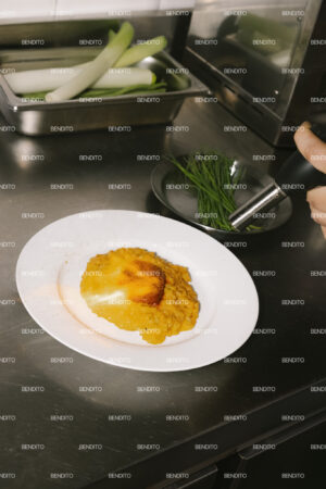 Melted sobrasada over saffron risotto in a stainless steel kitchen.