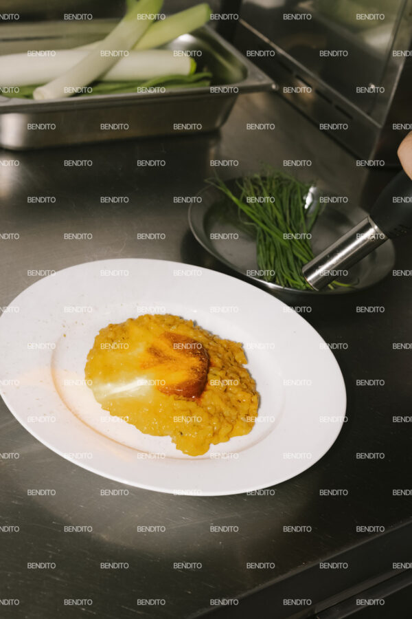 Tight crop of melted sobrasada over saffron risotto in a stainless steel kitchen.