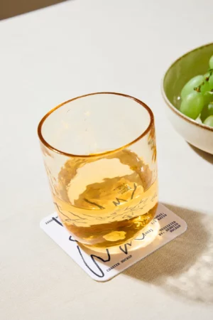 Amber drink glass resting on a Holy Water-themed coaster mockup, styled as a miracle certificate.