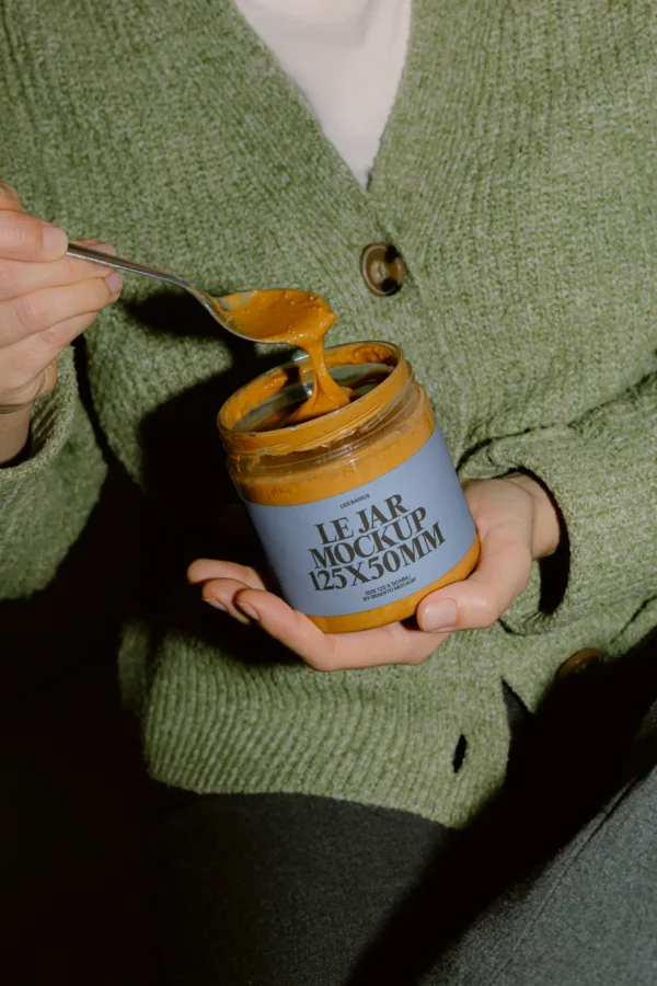 Glass jar mockup filled with thick spread, held in hands, with a soft blue label—perfect for branding nut butters, sauces, or food products.