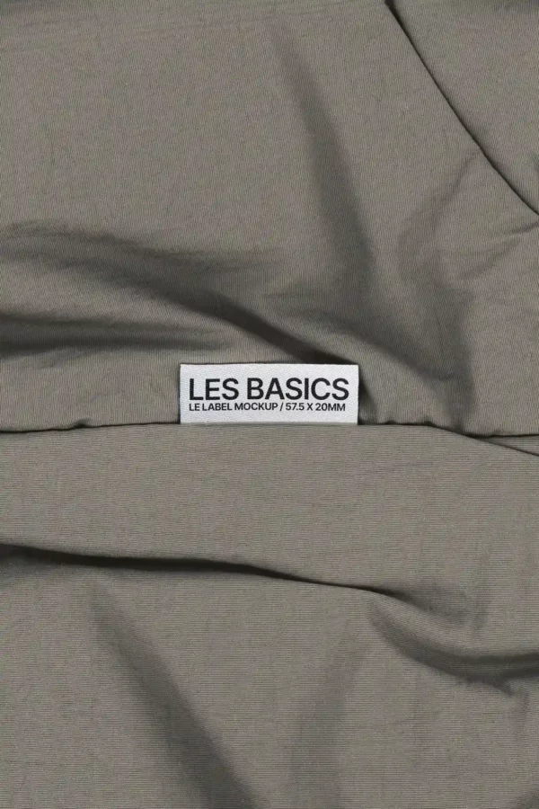 Fabric label mockup sewn onto gray cotton textile, sized 57.5 x 20 mm, ideal for showcasing clothing brand tags or garment labels.