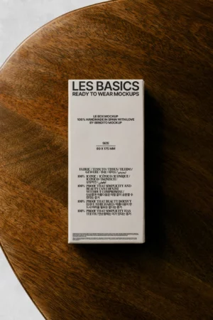 A rectangular mockup box labeled LES BASICS READY TO WEAR rests on a wooden surface, displaying product details and fabric composition in black text on a cream background.