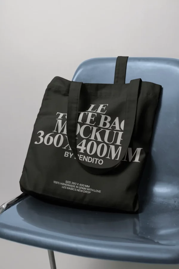 A black tote bag mockup with bold white text sits on a blue plastic chair. The text highlights Tote Bag Mockup 360x400mm and provides additional details about the bag’s size and material.