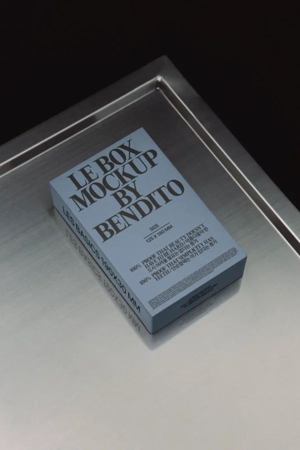 A blue rectangular box labeled LE BOX MOCKUP BY BENDITO sits on a brushed metal surface. The box features bold black text and design details in a minimalist style.