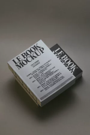 Two thick books titled LE BOOK MOCKUP are stacked on a plain surface, one white with black text on top and one black with white text slightly behind and to the right. Both books have a modern, minimalist design.